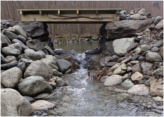 Vanninntak for et sideløp i et deltaområde til Vassbygdelva (Aurland) - etter modell fra skjematisk tegning over. Et rør skal sørge for vannføring også i ekstremsituasjoner, om vann i spalten skulle fryse.  Åpne inntaksgrøfter er enklere å passere for fisk og enklere å vedlikeholde enn rør. Rørinntak kan imidlertid dempe flomvannføring i større grad. 